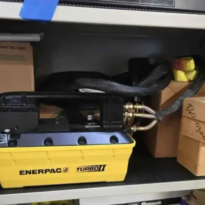 Sale Photo Thumbnail #133: Enerpac Turbo II air hydraulic pump, model PATG1102N, shown on a shelf alongside a Simplex bottle jack and wooden storage boxes.
