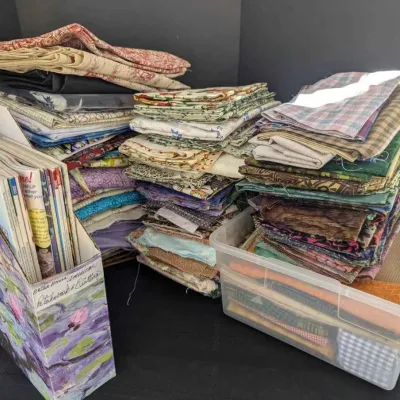 Sale Photo Thumbnail #54: Large collection of quilting and sewing fabric remnants in various patterns and colors, accompanied by a magazine holder filled with crafting publications.