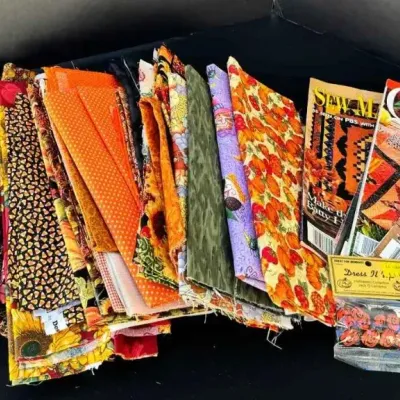Sale Photo Thumbnail #62: Assorted autumn-themed quilting fabric quarters, sewing magazines, and a small pack of decorative buttons.