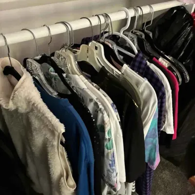 Sale Photo Thumbnail #102: Assorted women's clothing, including a fuzzy white vest, blouses, and shirts, hanging on a closet rod.