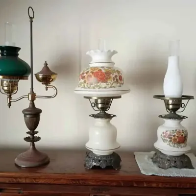 Sale Photo Thumbnail #155: Three vintage hurricane-style table lamps, including a brass student lamp with a green glass shade and two milk glass lamps featuring floral motifs.