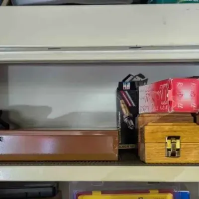 Sale Photo Thumbnail #103: Assorted tools and storage cases, including wooden boxes with brass latches, an Ingersoll Rand box, and a blue soft-sided bag, arranged on a metal shelf.