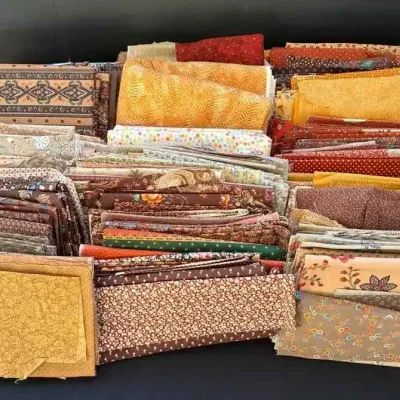 Sale Photo Thumbnail #29: Large assortment of folded quilting fabric remnants in warm tones, featuring various floral, geometric, and textured patterns.