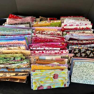 Sale Photo Thumbnail #27: Large assortment of folded quilting fabric quarters and remnants in a variety of colorful floral, novelty, and geometric patterns.