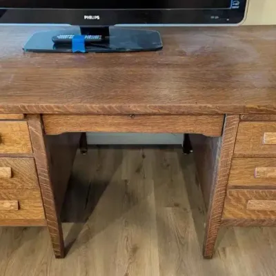 Sale Photo Thumbnail #194: Antique tiger oak double-pedestal desk featuring wooden drawer pulls and a central lap drawer, showing some surface wear on the top.