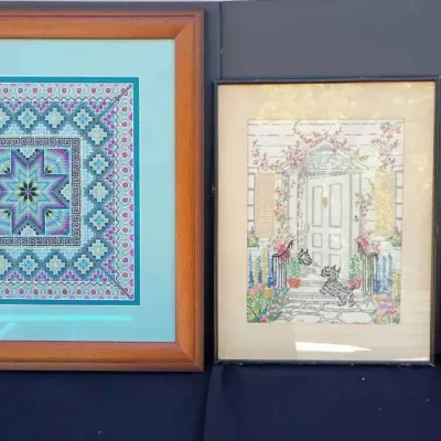 Sale Photo Thumbnail #182: Three framed wall art pieces, including a geometric needlepoint in a wooden frame, a framed illustration of a house entrance with dogs, and a Native American-style sand painting on a burlap-wrapped board.