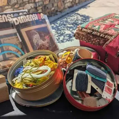 Sale Photo Thumbnail #65: Assorted sewing and needlework supplies, including embroidery floss in tins, Dimensions needlecraft kits, hoops, and a fabric-covered sewing basket.