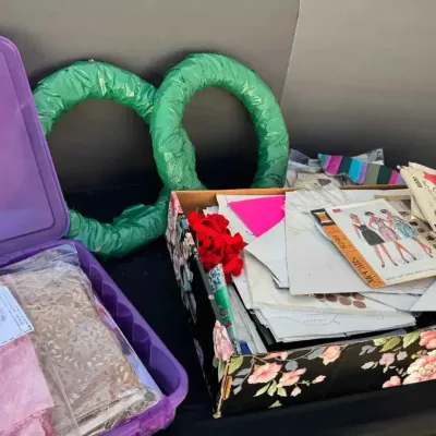 Sale Photo Thumbnail #71: Assorted crafting and sewing supplies, including vintage McCall's sewing patterns, fabric remnants in a purple plastic bin, and two green wrapped wreath forms.