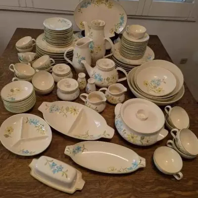 Sale Photo Thumbnail #179: Vintage Franciscan "Desert Rose" style dinnerware set featuring a delicate blue and yellow floral pattern, including plates, bowls, teacups, serving platters, a teapot, and a covered casserole dish.