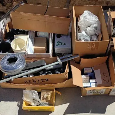 Sale Photo Thumbnail #72: Assorted plumbing and irrigation supplies, including PVC fittings, tubing, metal pipes, and boxed components, organized in cardboard boxes.