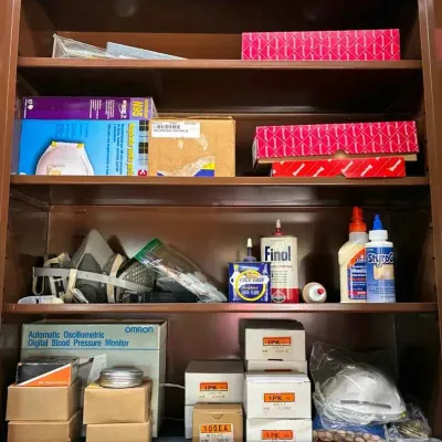 Sale Photo Thumbnail #104: Brown metal storage cabinet containing various workshop and household items, including N95 masks, a respirator, Finol lock fluid, wood glue, and an Omron digital blood pressure monitor.