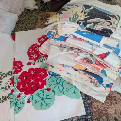 Sale Photo Thumbnail #88: Collection of vintage mid-century printed tablecloths and linens, featuring various floral, novelty, and holiday patterns.
