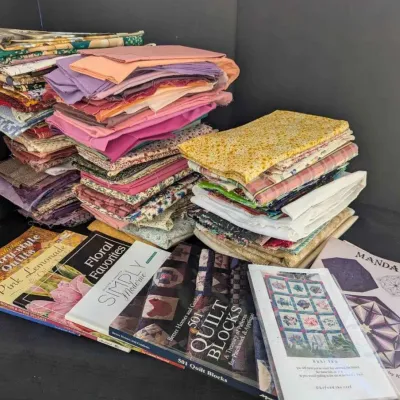 Sale Photo Thumbnail #36: A collection of quilting books and patterns, including "501 Quilt Blocks" and "Mandala," displayed alongside several stacks of colorful fabric remnants.