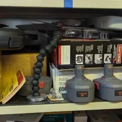 Sale Photo Thumbnail #108: Assorted Craftsman power tool accessories, including five rechargeable batteries, boxed items, and a flexible magnetic work light, arranged on a shelf.