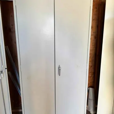 Sale Photo Thumbnail #49: Tall industrial metal storage cabinet in a light gray finish, featuring double doors with a central locking handle.
