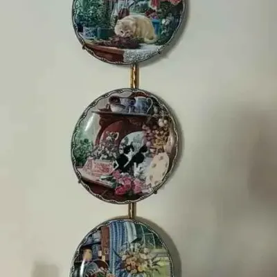 Sale Photo Thumbnail #199: Three-tier brass plate hanger with a decorative bow top, displaying three collectible cat-themed porcelain plates.