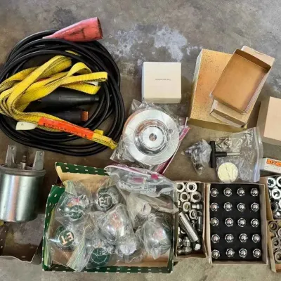 Sale Photo Thumbnail #119: Assorted automotive parts and hardware, including a Frantz oil cleaner full-flow adapter, a heavy-duty extension cord, a yellow tow strap, chrome lug nuts, and various packaged components.