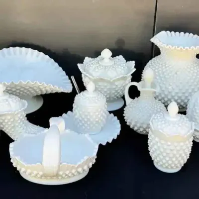Sale Photo Thumbnail #139: A collection of vintage Fenton hobnail milk glass tableware, including a large pitcher, decanter, ruffled bowls, and various lidded jars.