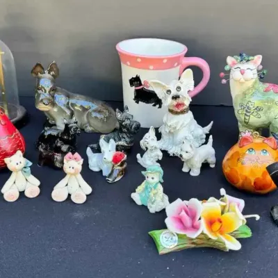Sale Photo Thumbnail #153: Collection of decorative figurines and collectibles, including Scottish Terrier figurines, a pink and white mug, teddy bears, and a colorful cat figurine.