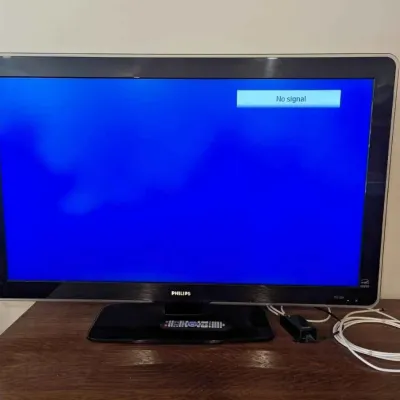 Sale Photo Thumbnail #189: Philips flat-screen television with a black bezel and stand, shown powered on with a "No signal" screen, accompanied by its remote control and cables.