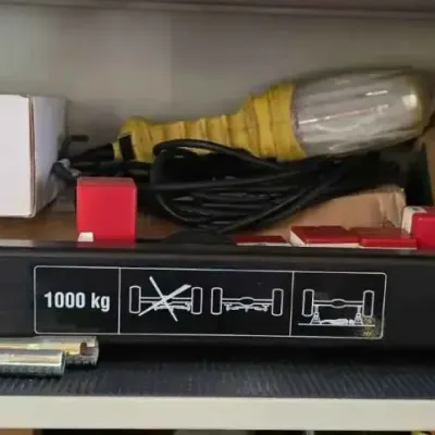 Sale Photo Thumbnail #132: A 1000 kg capacity cross beam adapter for a floor jack, shown on a shelf with a yellow work light and various boxes.