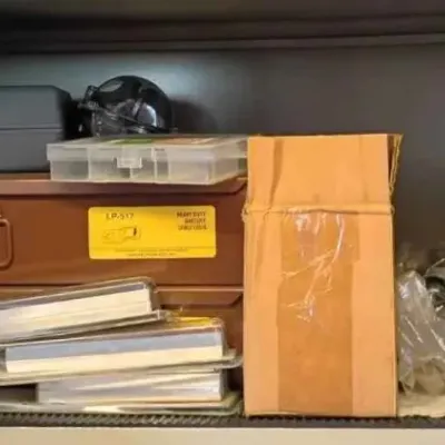 Sale Photo Thumbnail #113: Assorted tools and hardware, including a brown metal storage box, plastic carrying cases, and packaged items on a shelf.