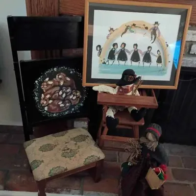 Sale Photo Thumbnail #190: Collection of folk art and country decor, including a framed print of Amish figures under a rainbow, a hand-painted folding chair with a rabbit motif, a small upholstered footstool, and handmade fabric dolls.