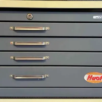 Sale Photo Thumbnail #117: Huot four-drawer metal tool chest in gray finish, featuring silver-tone handles and a top lock, shown stored on a shelf.