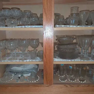 Sale Photo Thumbnail #156: Large collection of vintage glassware, including cut crystal wine glasses, goblets, tumblers, and serving pieces, neatly arranged inside a wooden cabinet.