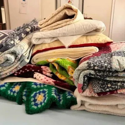Sale Photo Thumbnail #167: A large assortment of vintage blankets, quilts, and crocheted afghans in various colors and patterns, piled on a bed.