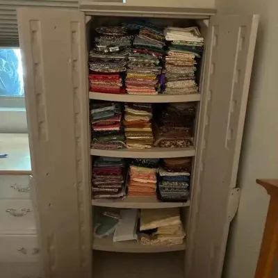 Sale Photo Thumbnail #191: A beige plastic storage cabinet with double doors, filled with neatly stacked fabric remnants and sewing supplies.