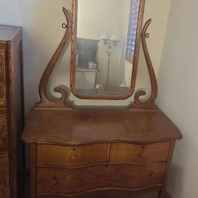 Sale Photo Thumbnail #98: Antique tiger oak vanity dresser featuring a serpentine front, three drawers with wooden knobs, and an attached swivel mirror supported by elegant curved harp brackets.