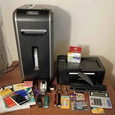 Sale Photo Thumbnail #86: Fellowes paper shredder and Canon all-in-one printer, displayed alongside various office supplies including a calculator, notebooks, tape dispensers, and scissors.