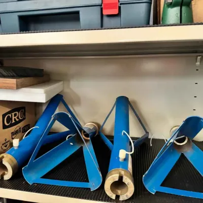 Sale Photo Thumbnail #127: Four blue metal outrigger bases or mounting brackets, showing some wear from use, stored on a workshop shelf.