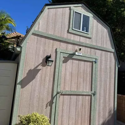 Sale Photo Thumbnail #19: Tuff Shed barn-style storage shed featuring light brown wood-textured siding, sage green trim, a single door, and a small upper window.