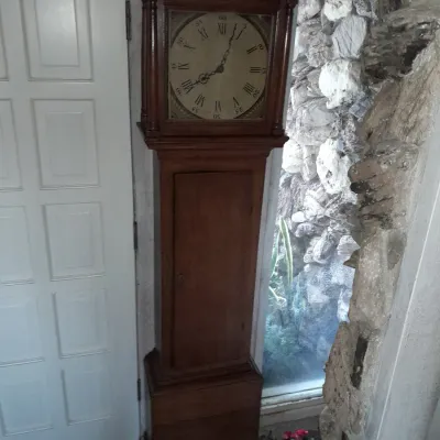 Sale Photo Thumbnail #4: Antique wooden grandfather clock featuring a simple, rustic case and a light-colored dial with Roman numerals.