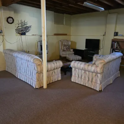 Sale Photo Thumbnail #179: Matching pair of traditional rolled-arm sofas with pastel patterned upholstery, accompanied by a matching armchair and ottoman set in a finished basement.