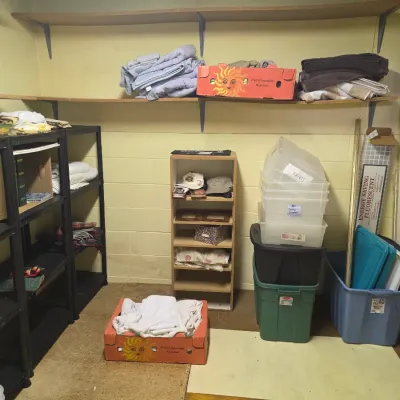 Sale Photo Thumbnail #203: Assorted household storage items, including plastic bins, shelving units, linens, and cardboard boxes, organized in a basement or storage room.