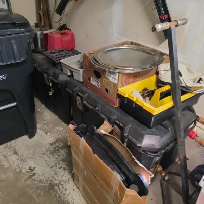 Sale Photo Thumbnail #164: Assorted garage items including large black plastic storage trunks, a hand truck, a yellow tool caddy, and various household goods.