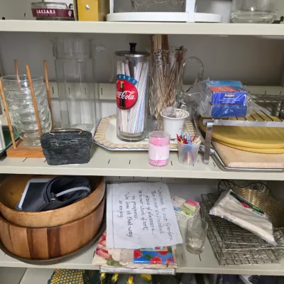 Sale Photo Thumbnail #137: Assorted vintage kitchenware and household items, including a Coca-Cola straw dispenser, wooden bowls, glassware, and a wire basket, arranged on metal shelving.