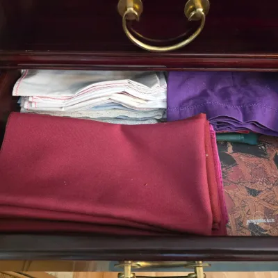 Sale Photo Thumbnail #17: Assorted vintage table linens, including cloth napkins and placemats in burgundy, purple, and white, stored inside a dark wood drawer.