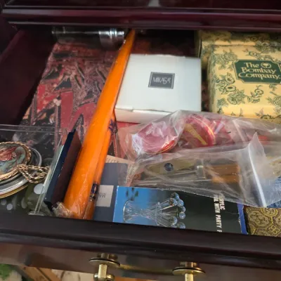 Sale Photo Thumbnail #15: Assorted small collectibles and gift items inside a wooden drawer, including a boxed item from The Bombay Company, a Mikasa box, and a decorative pocket watch.