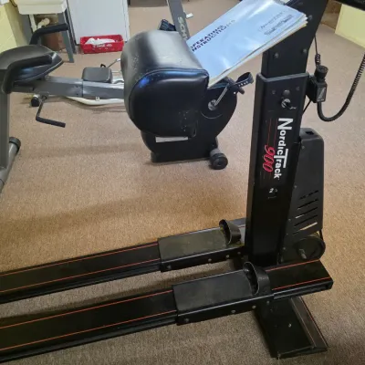 Sale Photo Thumbnail #194: NordicTrack 900 ski machine with operating instructions, shown alongside a recumbent exercise bike in a home gym setting.