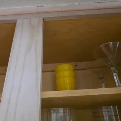 Sale Photo Thumbnail #133: Assorted glassware, including martini glasses and a stack of yellow plastic cups, stored inside a wooden kitchen cabinet.