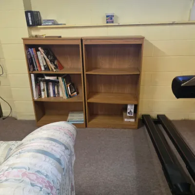 Sale Photo Thumbnail #193: Pair of matching oak-finish laminate bookcases with adjustable shelves, shown in a basement setting alongside a NordicTrack treadmill.