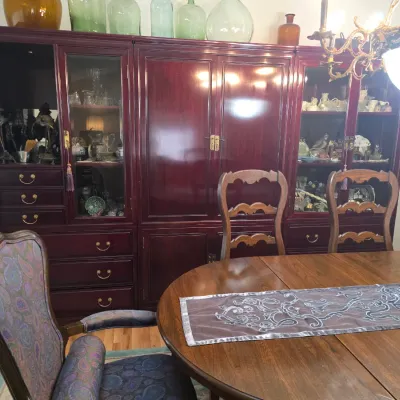 Sale Photo Thumbnail #4: Large Asian-style mahogany-finish wall unit with glass display cabinets, brass hardware, and central storage doors, shown behind a wooden dining table and chairs.