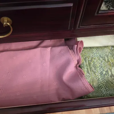 Sale Photo Thumbnail #18: Assorted folded fabrics, including a textured pink material and a green snakeskin print, stored inside a dark wood drawer.