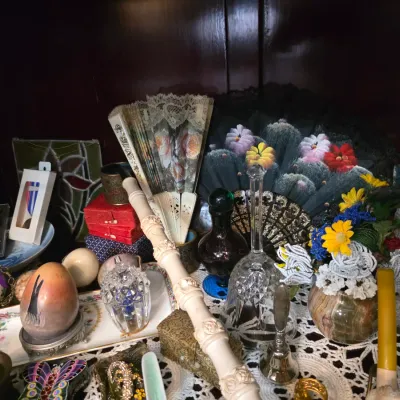 Sale Photo Thumbnail #43: Assortment of vintage collectibles including decorative hand fans, crystal glassware, hand-painted eggs, and a carved ivory-style flute displayed on a lace tablecloth.