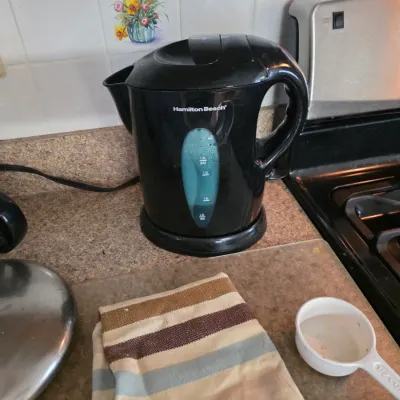 Sale Photo Thumbnail #127: Hamilton Beach black plastic electric kettle with a water level window, shown on a kitchen counter.