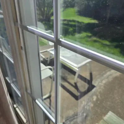 Sale Photo Thumbnail #90: View through a multi-pane glass sliding door looking out onto a patio with outdoor furniture.